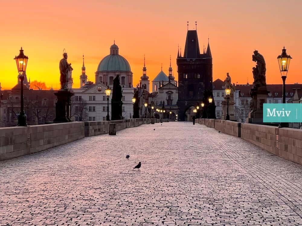 a stone walkway with a statue and buildings in the background with Charles Bridge in the background